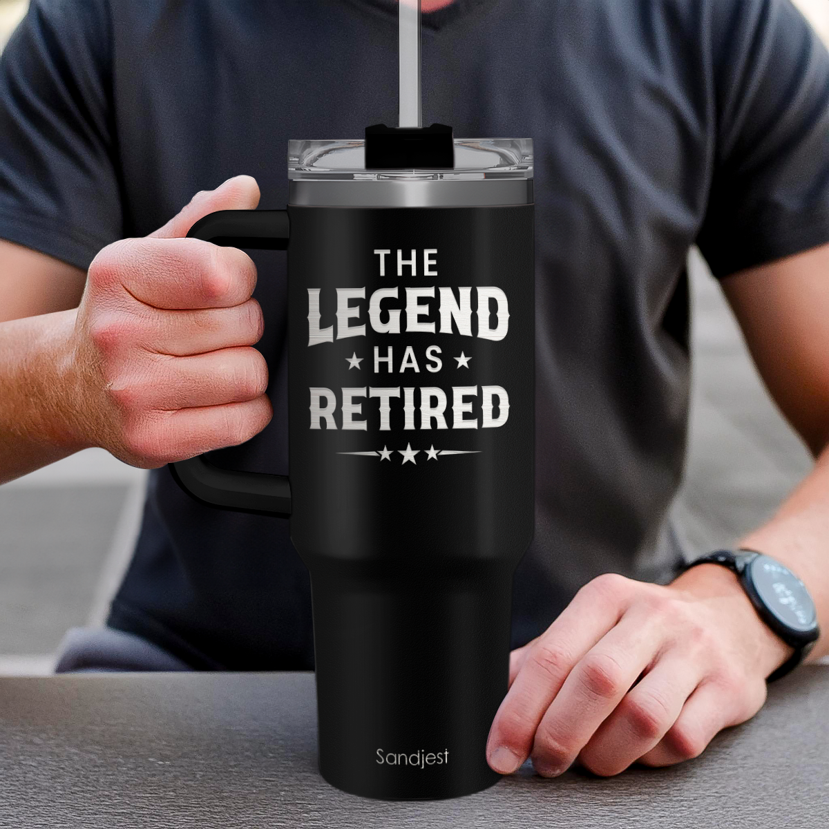 Hand holding black 40oz tumbler with handle, “The Legend Has Retired” front graphic