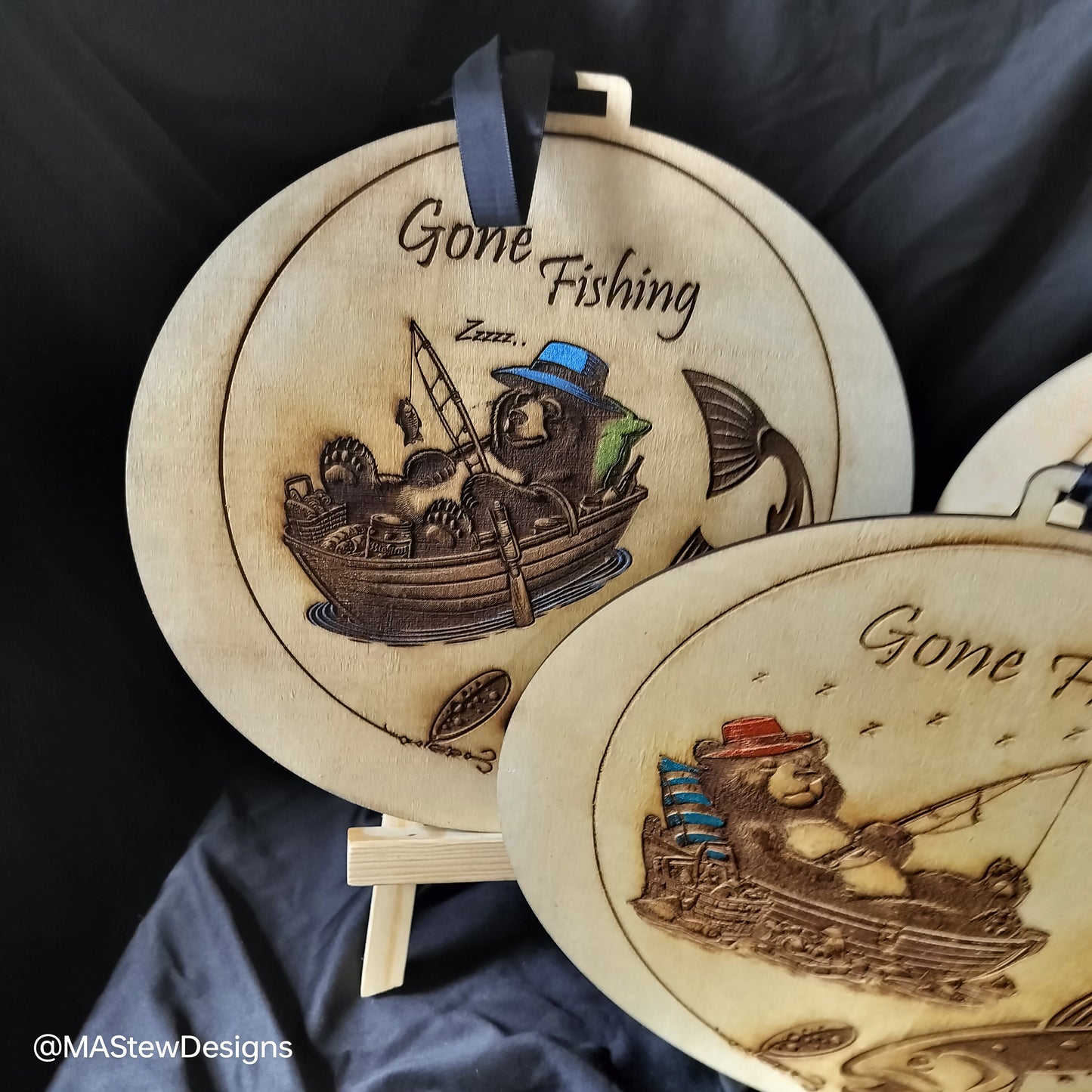 Two round wood wall hangers engraved 'Gone Fishing' with fishing boat and fish scenes