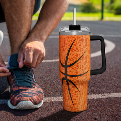 Orange basketball tumbler with black handle, standing on outdoor pavement