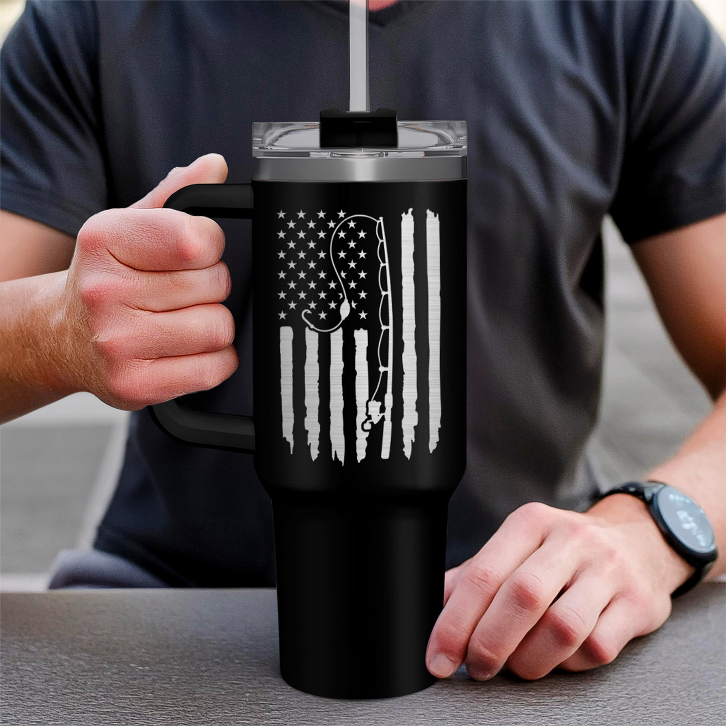 Black 40oz tumbler with handle and patriotic graphic, hand holding it