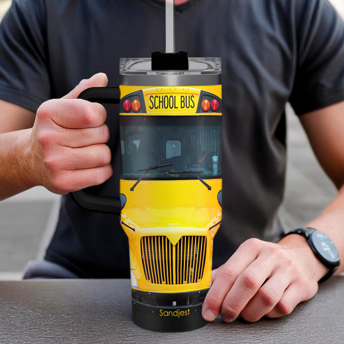 Yellow school bus graphic tumbler with black handle, clear lid, held in hand