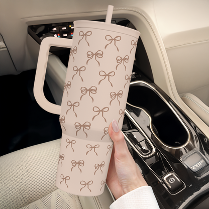 Light tan bow-pattern travel tumbler with handle and straw, held near a car console