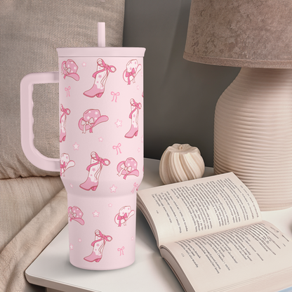 Pink 40oz cowgirl tumbler with handle and straw, standing on table with cowgirl pattern
