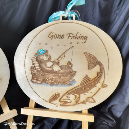Round wood wall hanger with 'Gone Fishing' engraved fishing boat and fish, blue ribbon