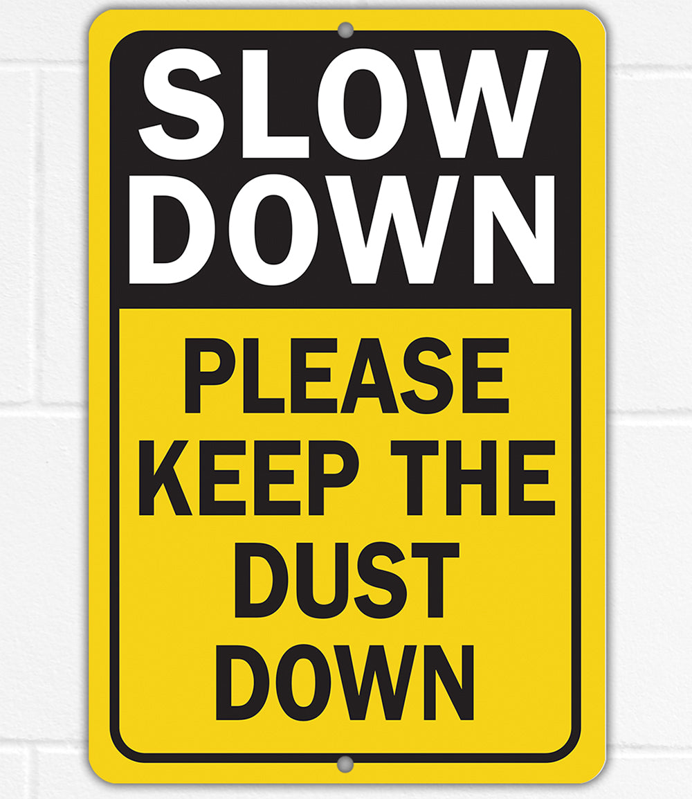 Yellow metal sign reading “SLOW DOWN” and “PLEASE KEEP THE DUST DOWN”