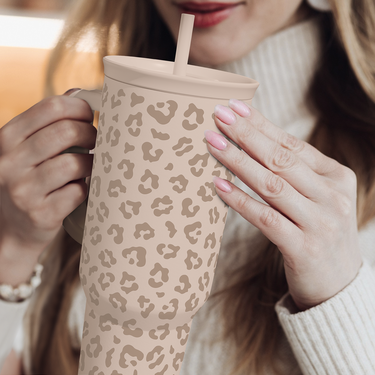 Leopard-print 40 oz tumbler with handle and straw, beige tan spots held by hands