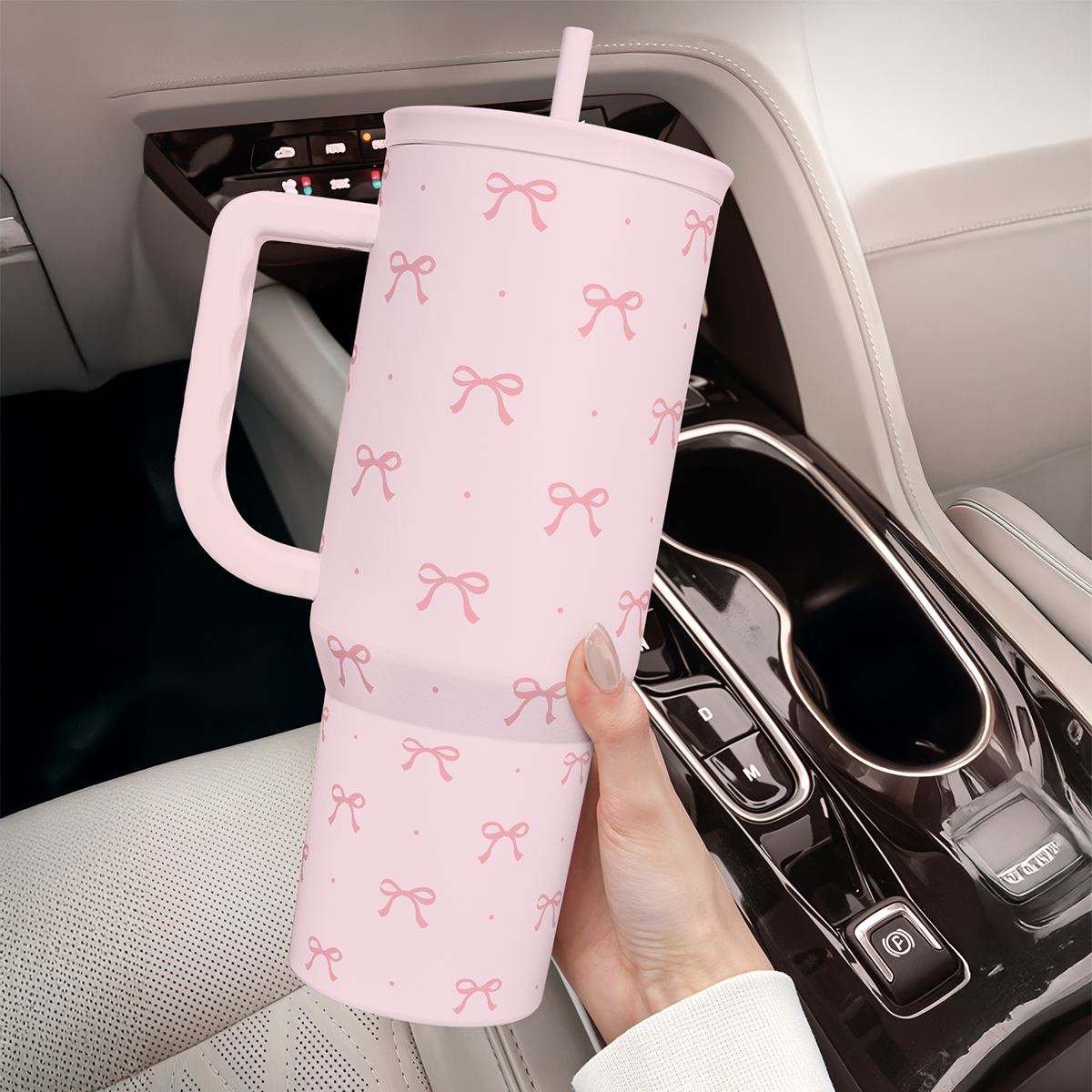 Pink tumbler with handle held near car seat, bow pattern and straw