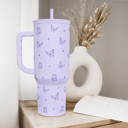 Lilac 40oz tumbler with handle and straw, butterfly pattern, on a wooden shelf.