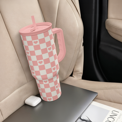 Coral checker heart tumbler with handle and straw lid, standing near seat