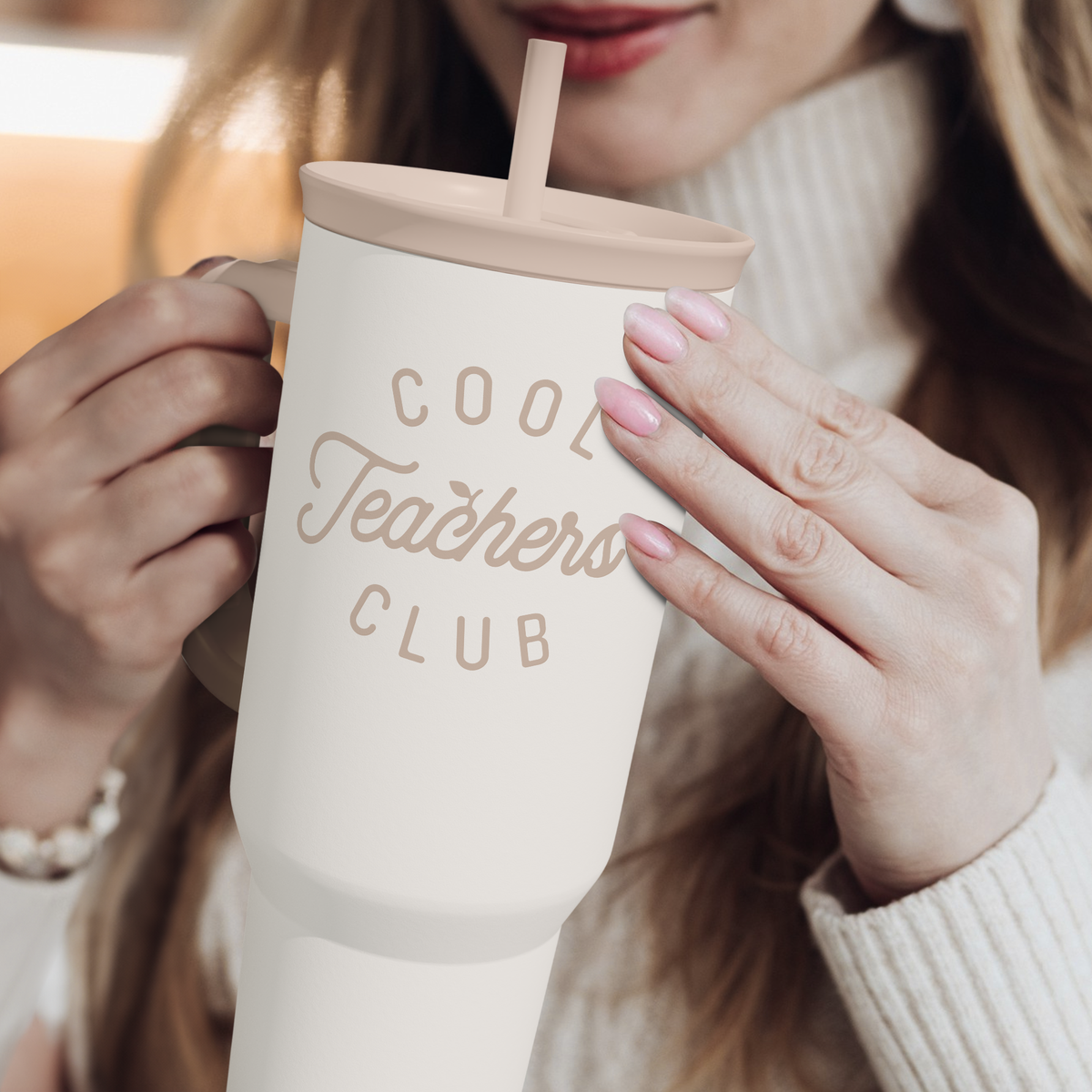 White tumbler with straw and “Cool Teachers Club” logo, held in hands