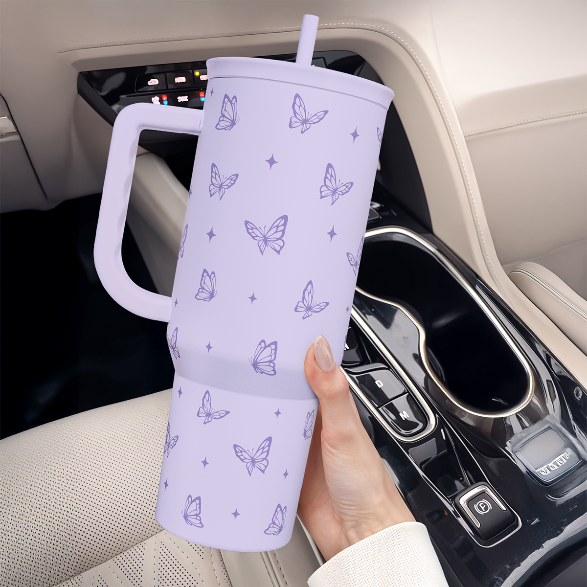 Lilac butterfly-print tumbler with handle and straw, held upright near car dashboard.