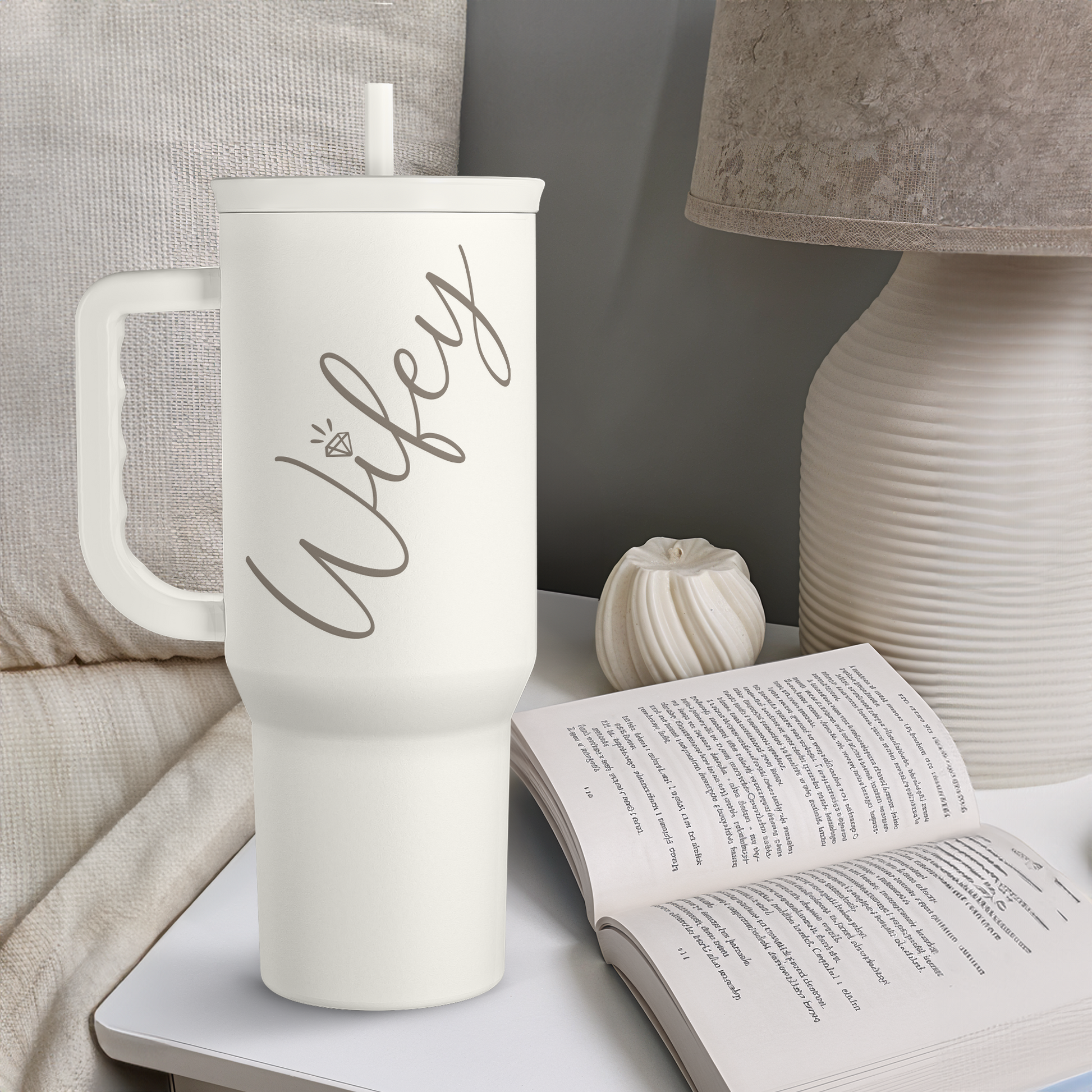 White tumbler with handle and slide lid straw, wife print, on a bedside table