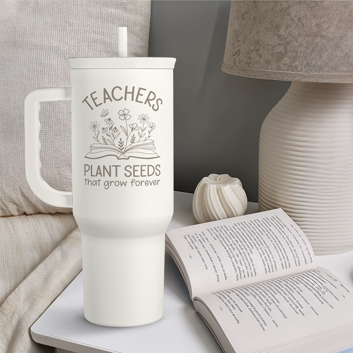 White 40oz tumbler with handle, plant seeds graphic and straw, next to open book