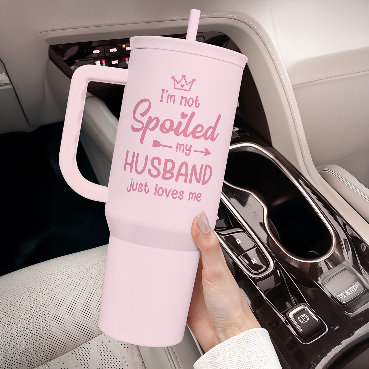 Pink tumbler with handle and straw set in a car cup holder; “I’m not Spoiled” design