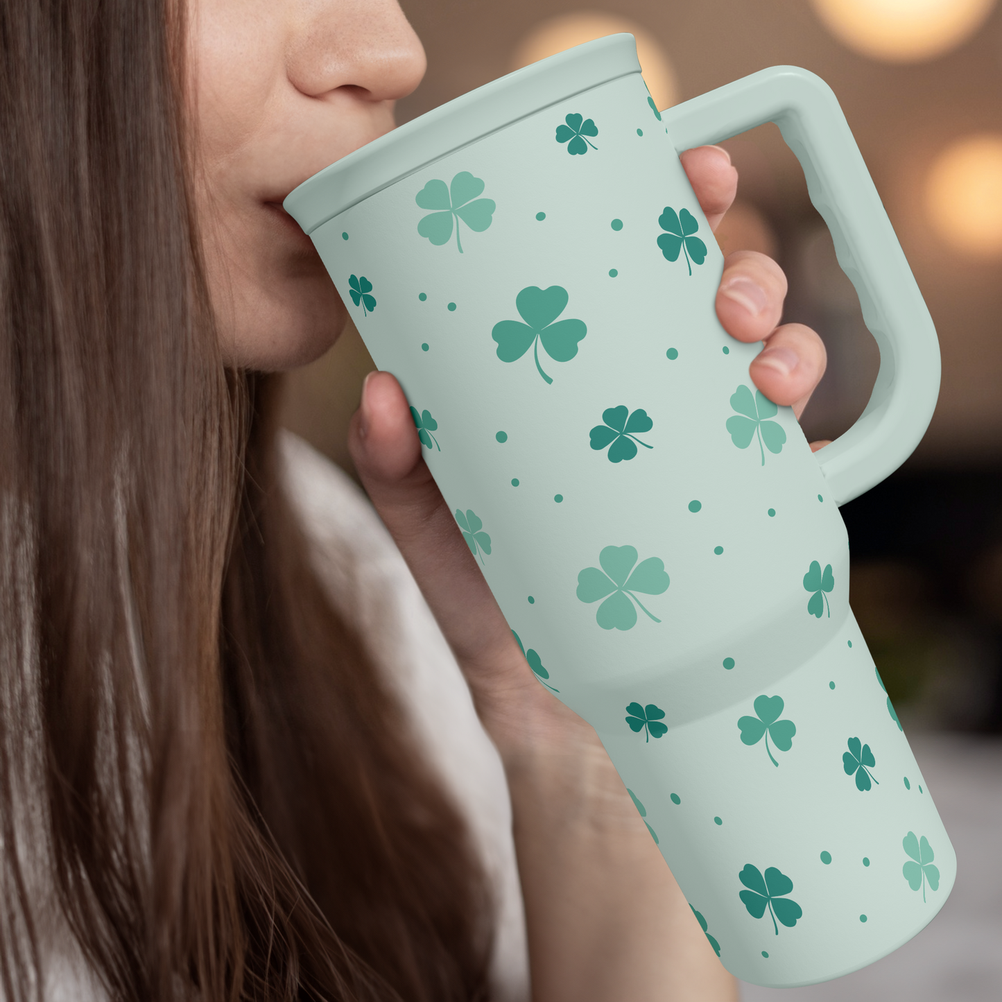 Mint green 40oz slide tumbler with handle, shamrock clover pattern, held to drink