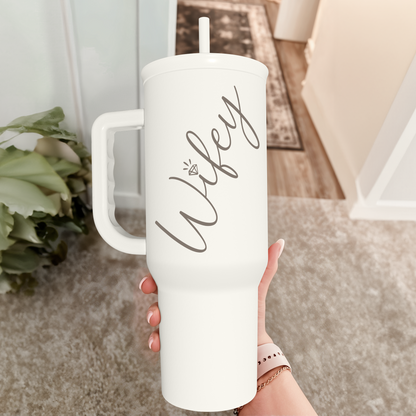 White tumbler with handle and straw, wife print, held in a hand