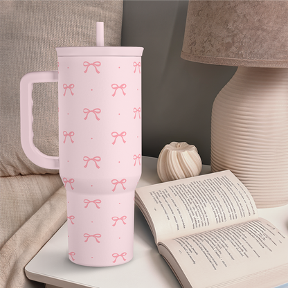 Pink tumbler with handle standing upright, bow print design