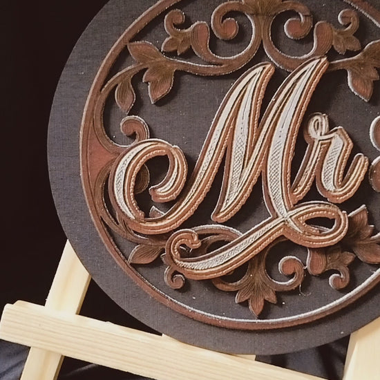 8x8 round Mr and Mrs chair signs. Black back ground with a mahogany leaf scroll pattern. 3 layers, backboard, scroll design,  Mr or Mrs on top to give a 3D look. 