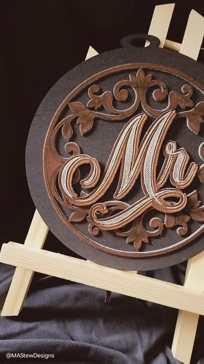 8x8 round Mr and Mrs chair signs. Black back ground with a mahogany leaf scroll pattern. 3 layers, backboard, scroll design,  Mr or Mrs on top to give a 3D look. 