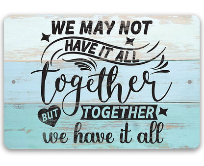 Light blue metal wall sign with 'We may not have it all' quote in black script.